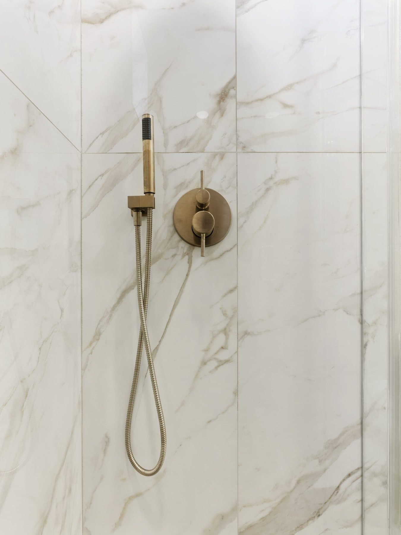 Small bathroom remodel: brushed-gold hand shower on marble-look tile